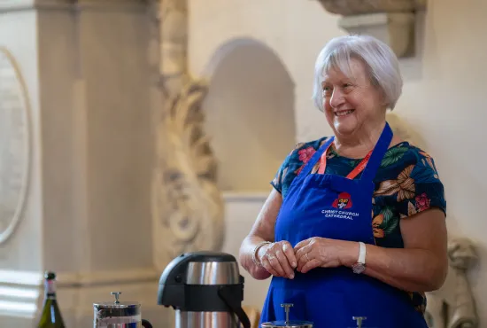 Susan Pagano, a member of the Cathedral refreshments team, wearing her blue cathedral apron and ready to offer you a mug of coffee with a smile