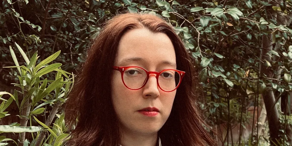 Photo of a woman with glasses and curly shoulder length brown hair, wearing a suit.