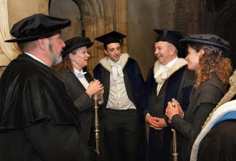 Oxford University's Senior and Junior Proctors are joined by the University bedels, carrying their staves. All are dressed in dark suits, white tie, and mortarboards.