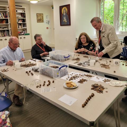 Cathedral Volunteers count coins from the cloisters fountain. The tables in the priory room are covered in neat stacks of coins, surrounded by four volunteers hard at work. 