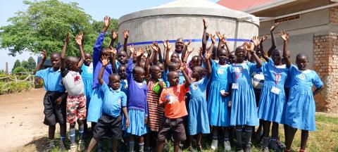 A group of school children in Uganda stand in front of their new rainwater harvesting tank