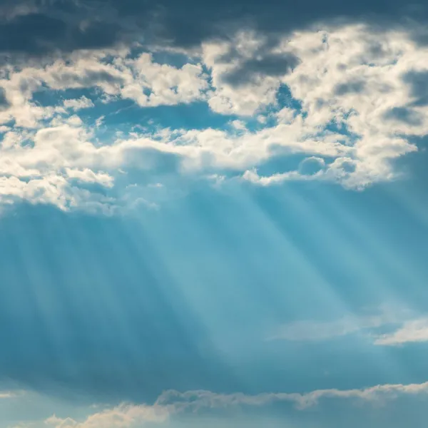 Sunlight bursts through the clouds against a blue sky